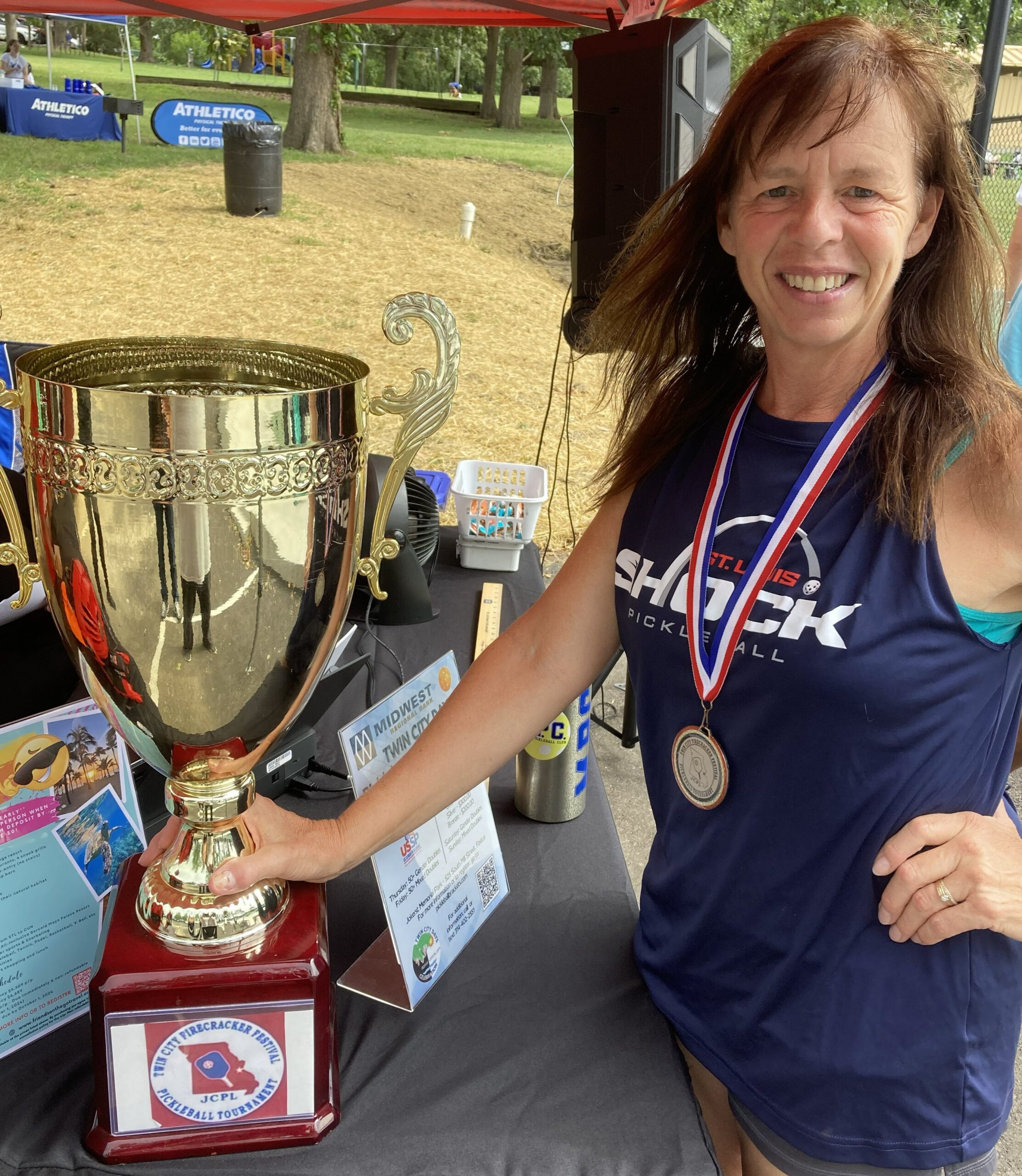 Cindy Butler smiling beside a large pickleball tournament trophy