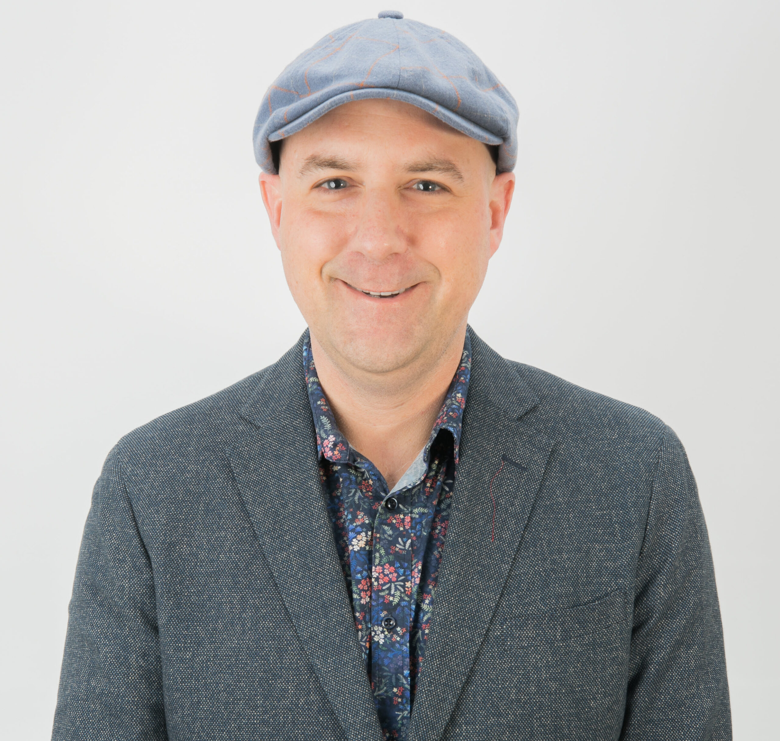 Luke Pivac smiling in a blue flat cap and blazer against a light background
